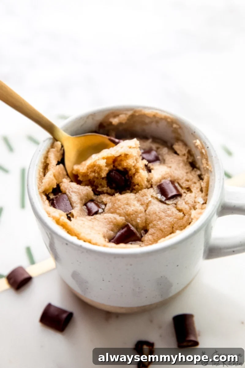 Close up of a spoon resting in a vegan chocolate chip mug cake, showing its moist texture and melted chocolate chips.