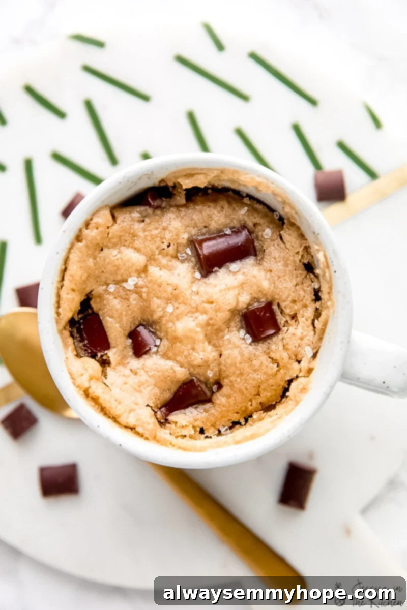 Overhead view of a chocolate chip mug cake next to a gold spoon, showcasing its perfect rise and golden-brown top.