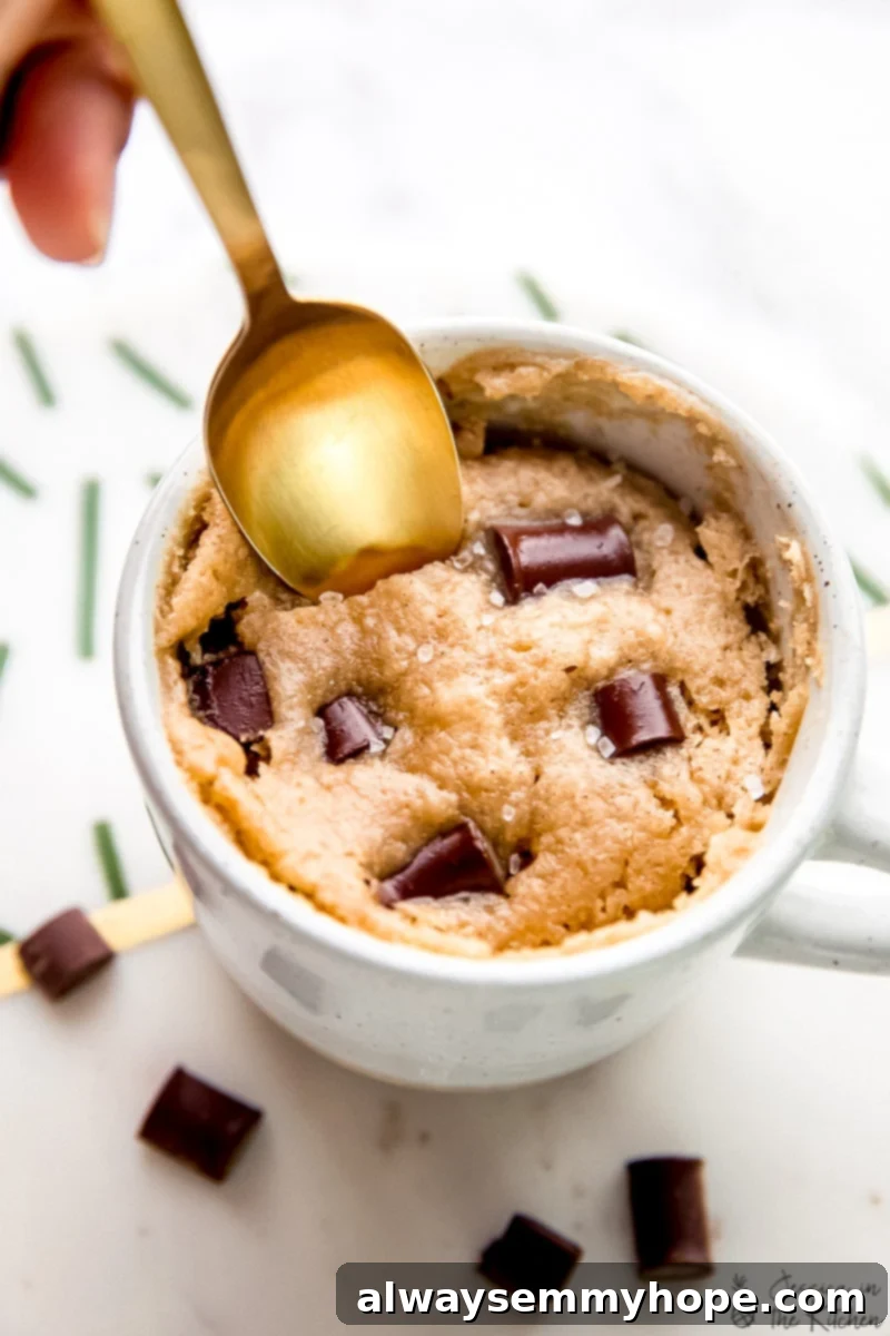 A spoon dipping into a vegan chocolate chip mug cake, highlighting the melted chocolate.