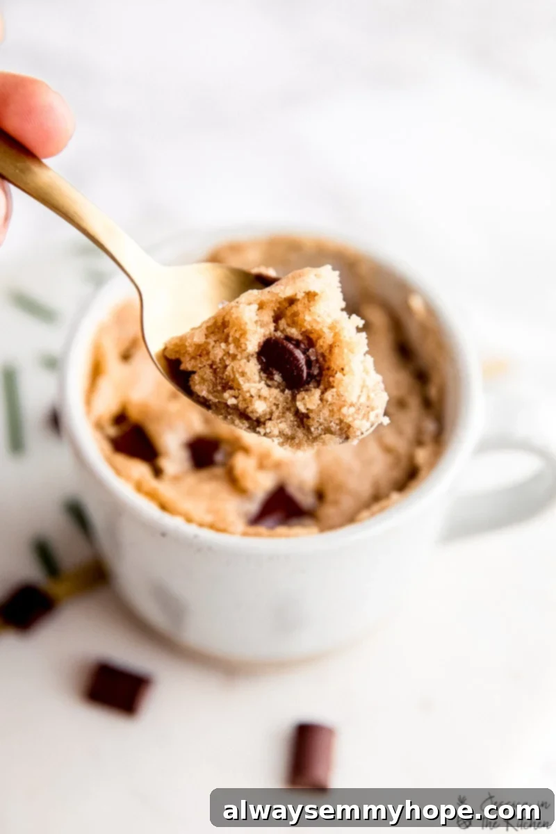 Close up of a spoonful of tahini chocolate chip mug cake with a mug in the background, showing the soft interior.
