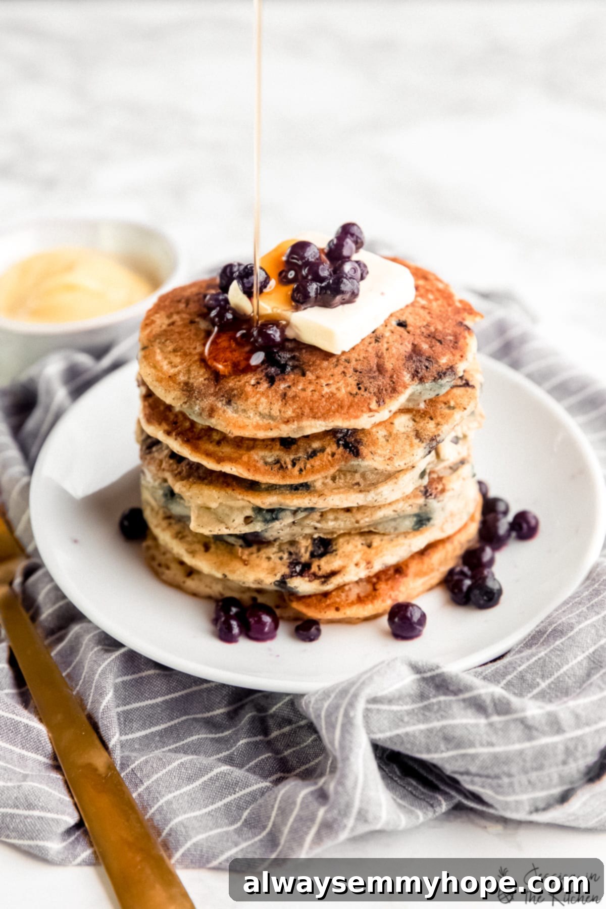 A tall stack of fluffy vegan blueberry pancakes generously drizzled with golden maple syrup, ready to be enjoyed.