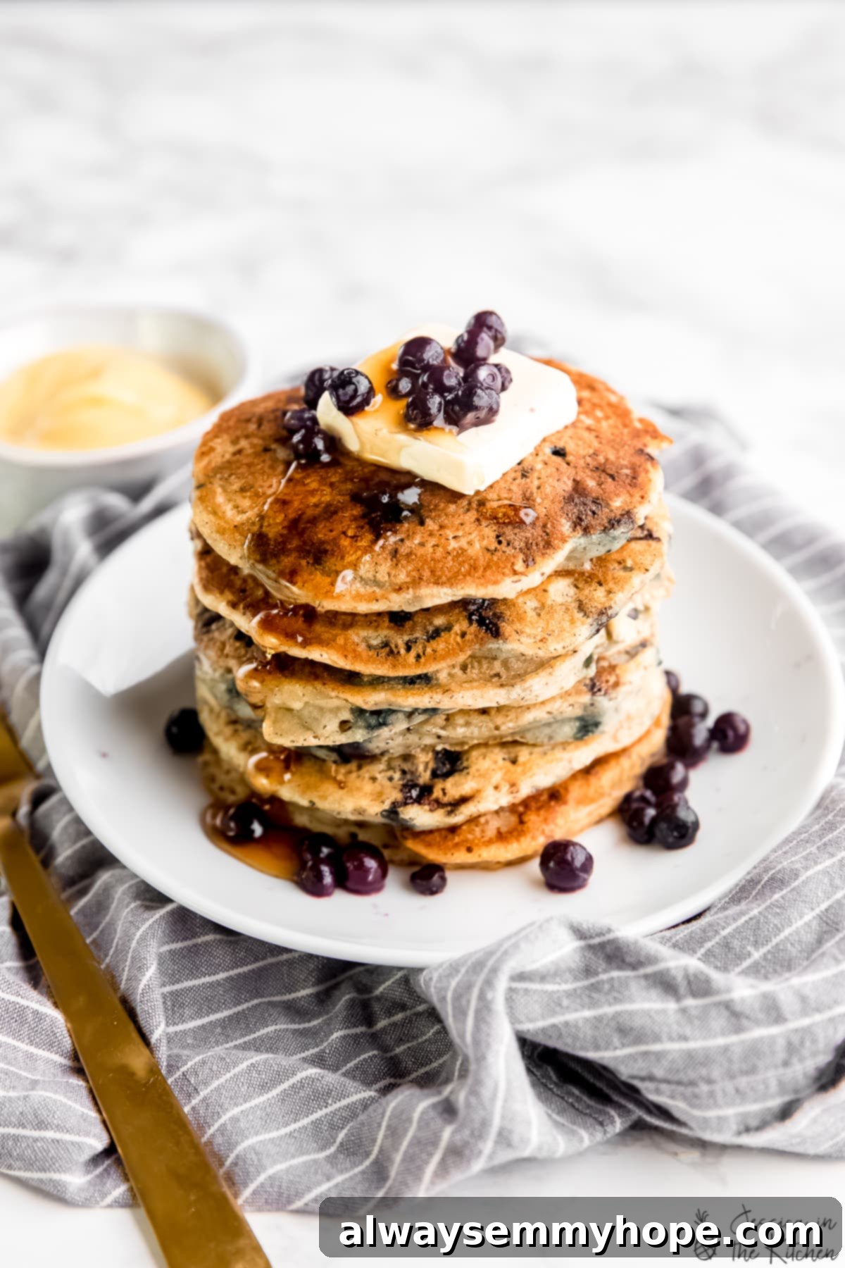 A close-up shot of a stack of fluffy vegan blueberry pancakes adorned with a dollop of vegan butter and generous maple syrup.