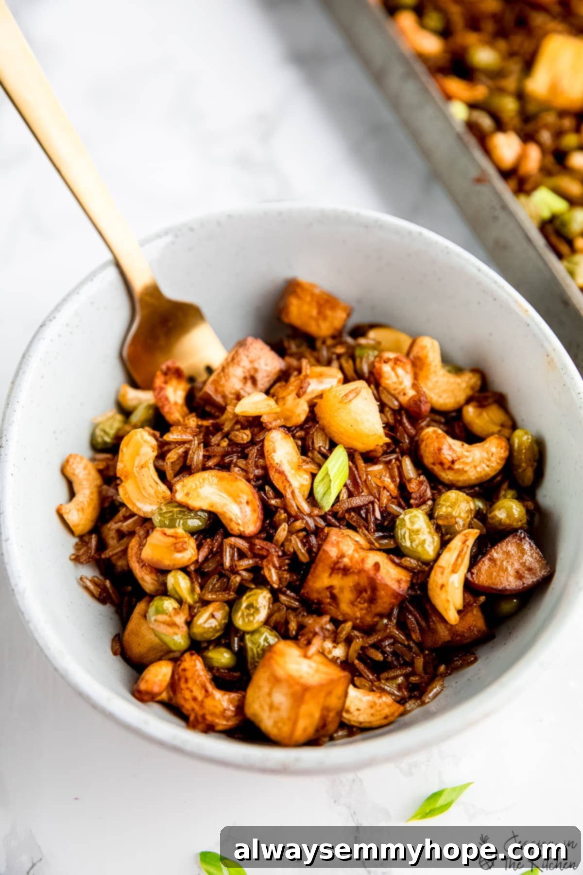 Experience the best vegan fried rice ever, baked to crispy, chewy perfection on a single sheet pan! Delicious bowl of crispy sheet pan vegan fried rice with tofu and cashews, ready to be enjoyed.