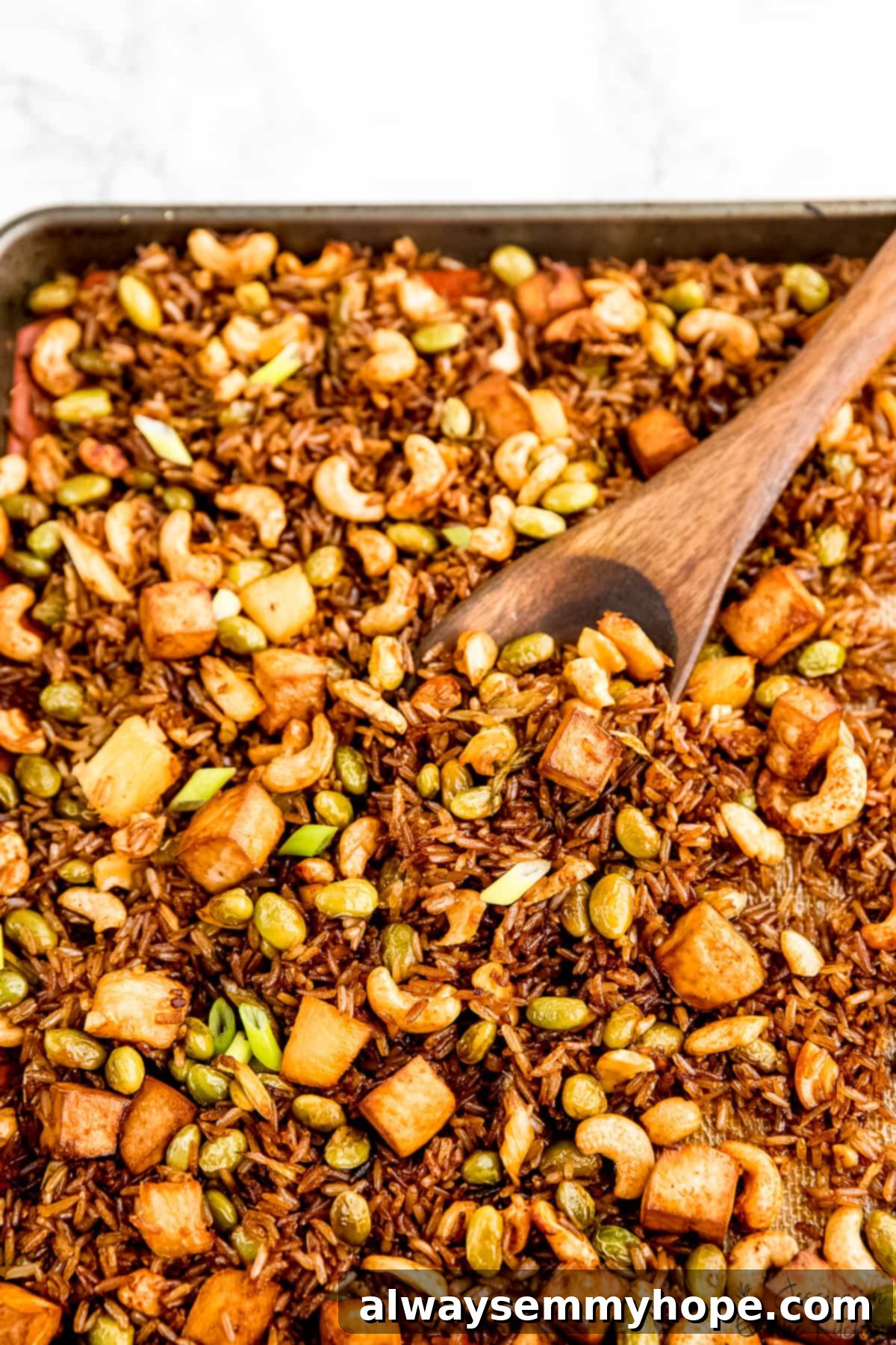 Witness the simplicity: perfectly mixed vegan fried rice spread on a sheet pan before baking to crispy perfection! Overhead view of vibrant vegan fried rice with colorful vegetables and tofu spread on a sheet pan, ready for baking.