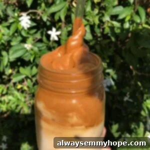 Dalgona Kahve Nasıl Yapılır Püf Noktalarıyla 5 Whipped coffee in a mason jar being twirled out with a straw, showing the thick, creamy texture.