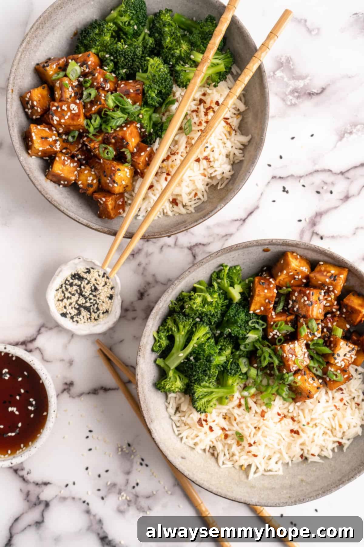 Two bowls of General Tso Tofu with white rice and broccoli, garnished with sesame seeds and green onions