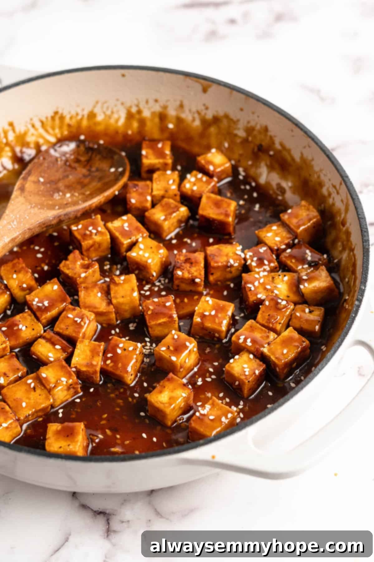 General Tso Tofu in a skillet with a wooden spoon, garnished with sesame seeds and scallions