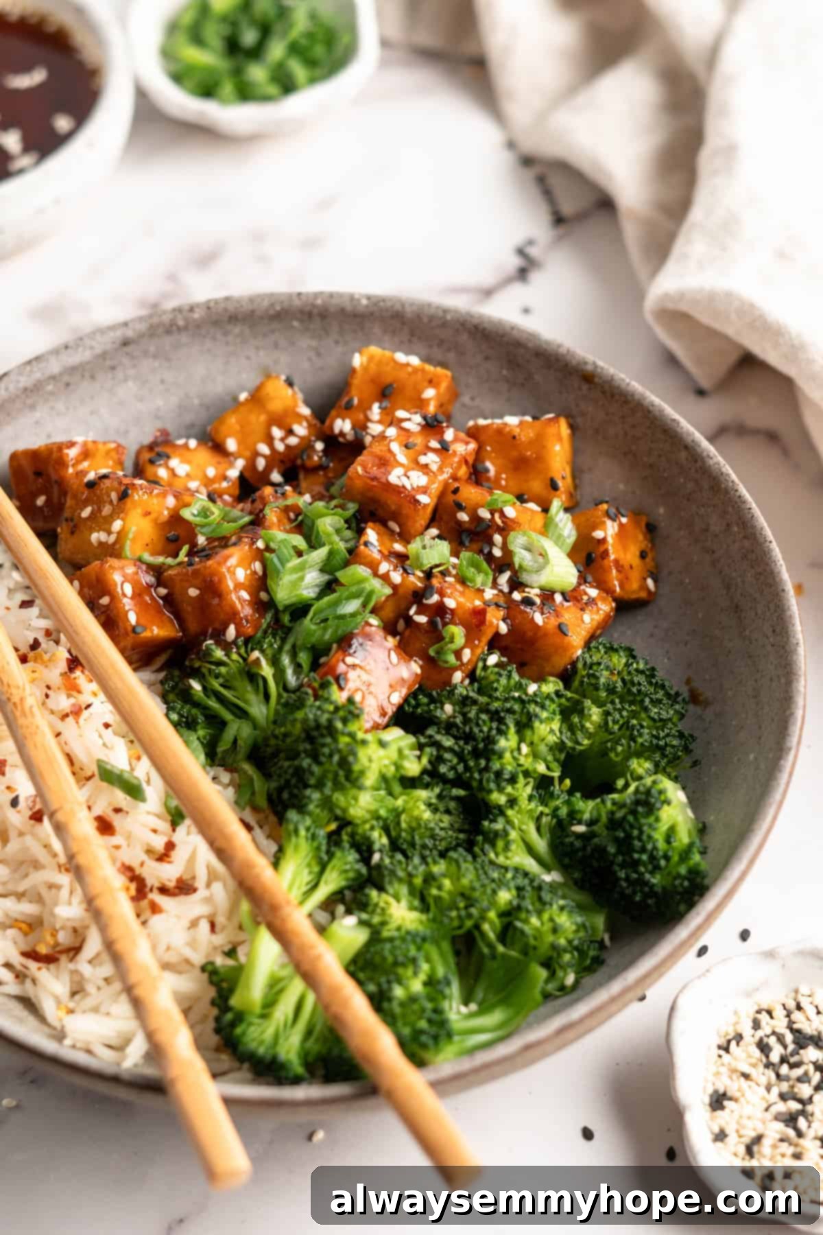 Bowl of General Tso Tofu with broccoli and white rice, garnished with sesame seeds and green onions