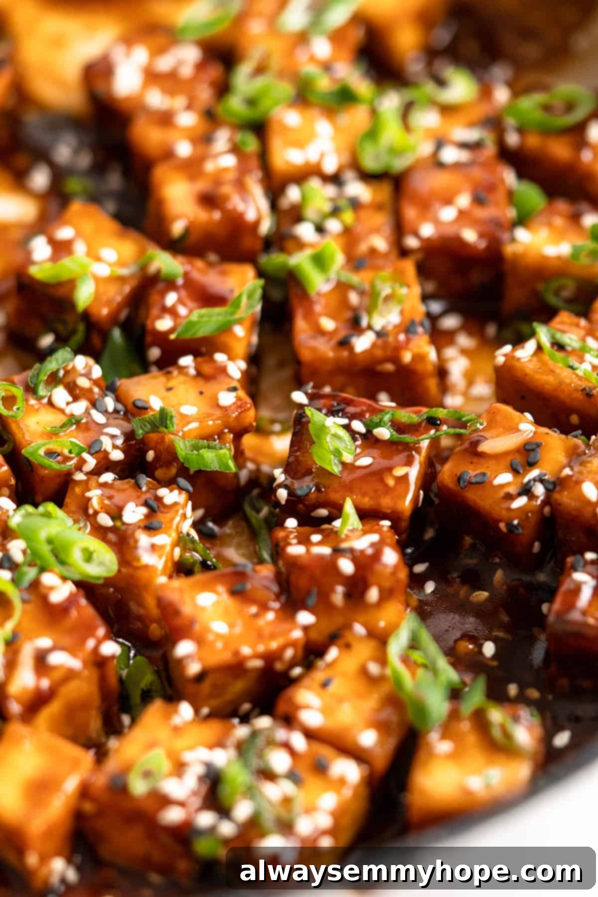 Closeup of General Tso Tofu topped with sesame seeds and scallions in a bowl