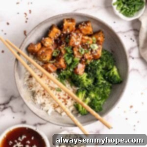 General Tso Tofu in bowl with rice and broccoli with chopsticks and garnishes