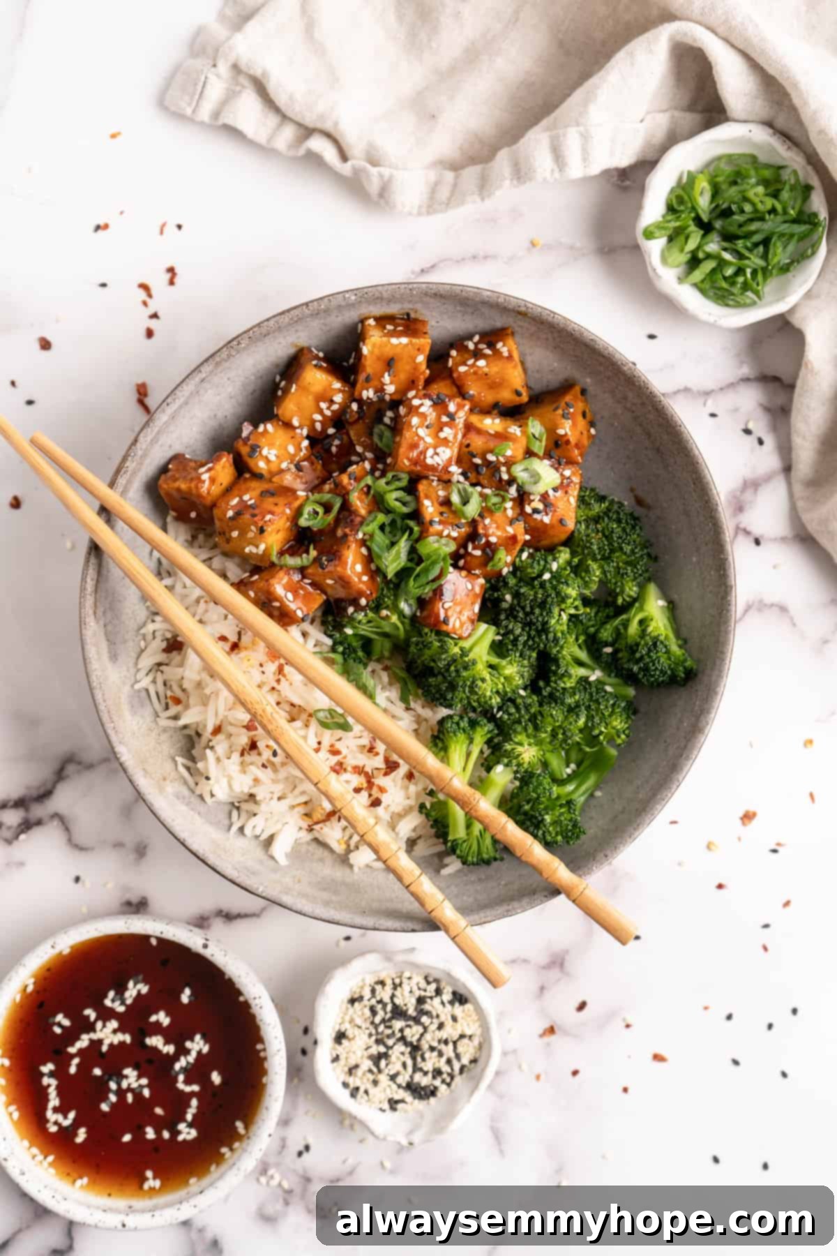 General Tso Tofu in bowl with rice and broccoli with chopsticks and garnishes