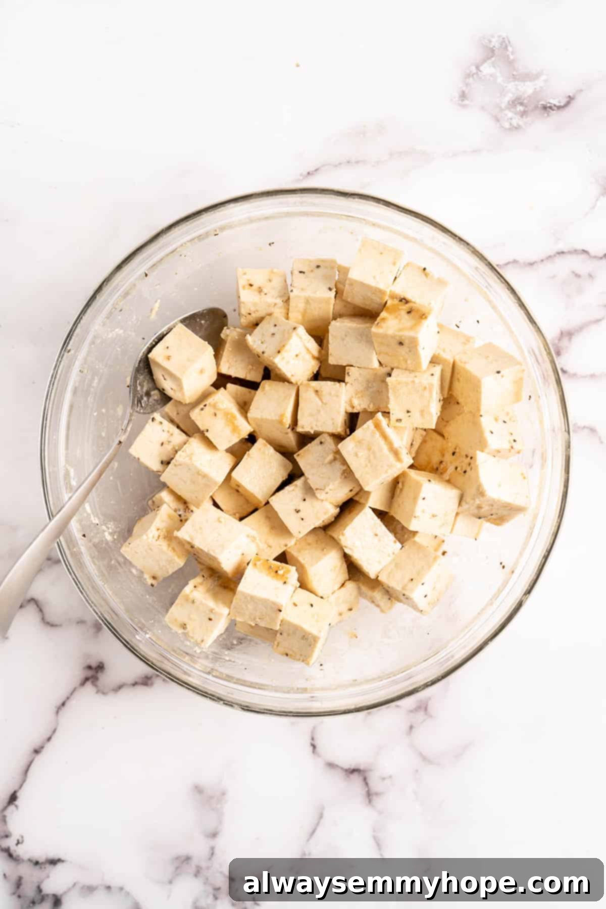Tofu being coated with seasonings and cornstarch in a glass mixing bowl