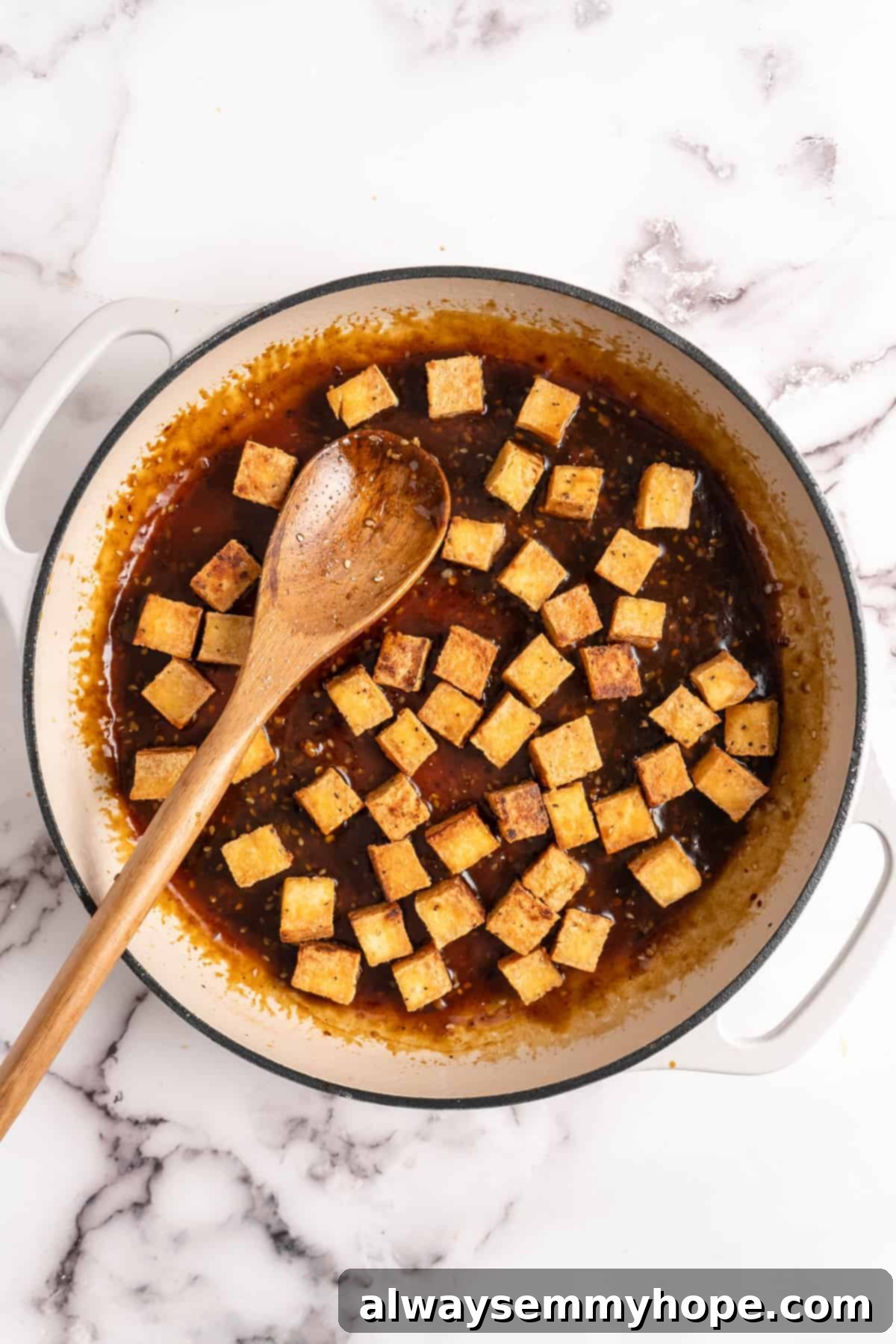 Crispy tofu being added to the simmering General Tso sauce in a pan