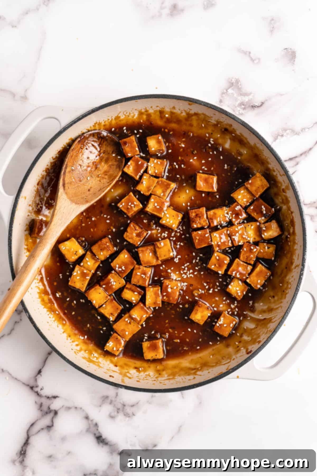 General Tso Tofu fully coated in sauce in a pan with a wooden spoon