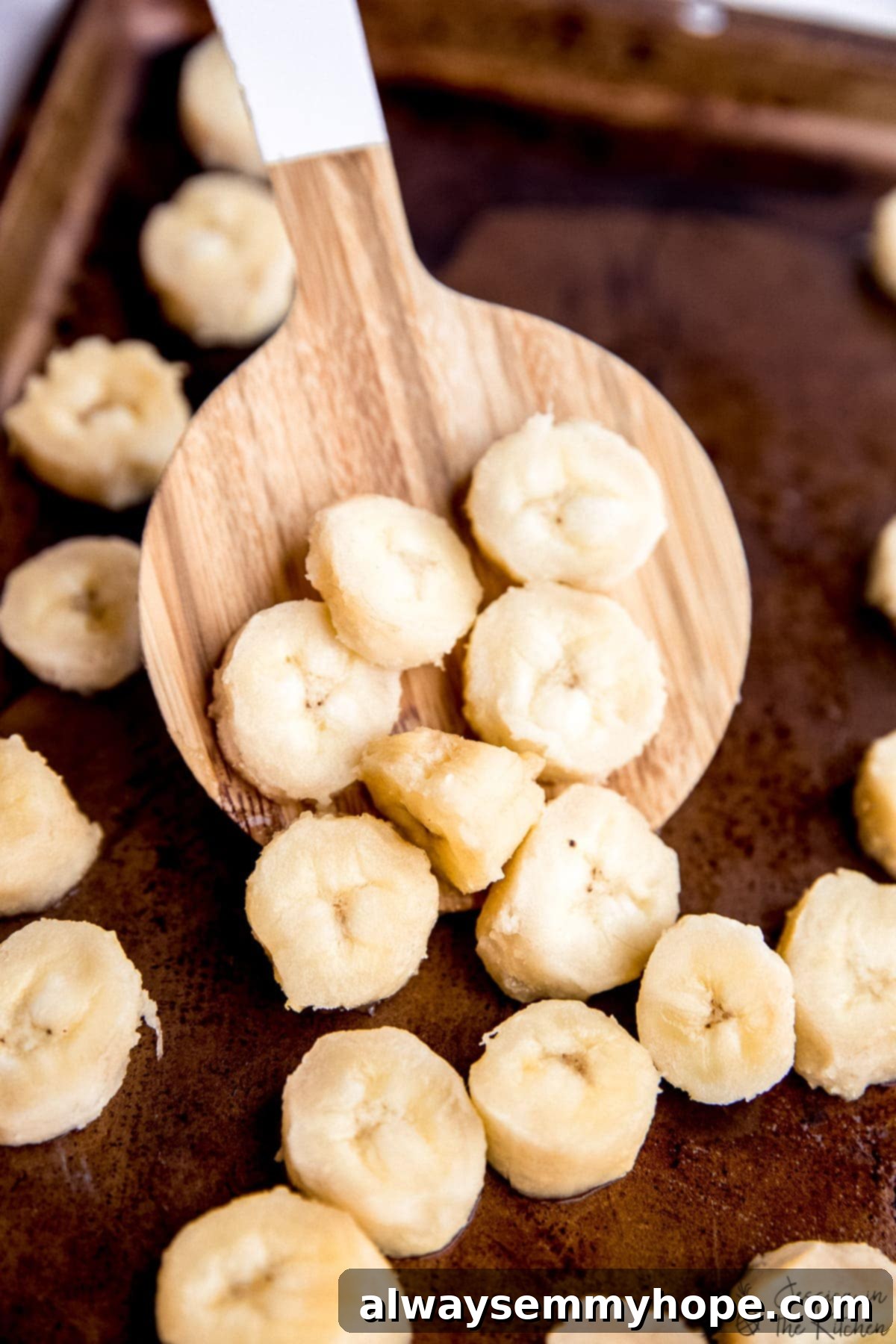 Frozen banana slices evenly spread on a baking sheet, ready for transfer.