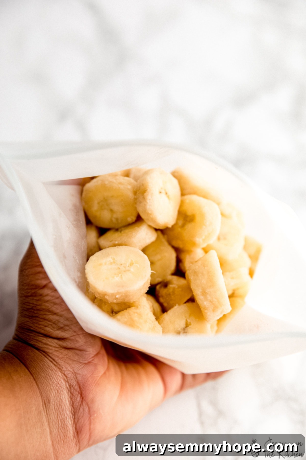 A hand holding a ziplock bag filled with perfectly frozen banana slices.