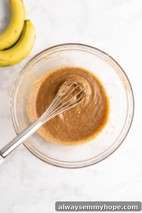 Overhead view of banana bread batter in glass bowl with whisk