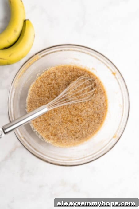Overhead view of wet ingredients for banana bread in glass bowl with whisk