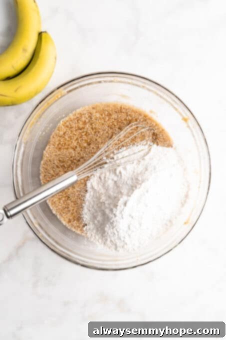 Overhead view of dry ingredients added to banana bread batter in glass bowl