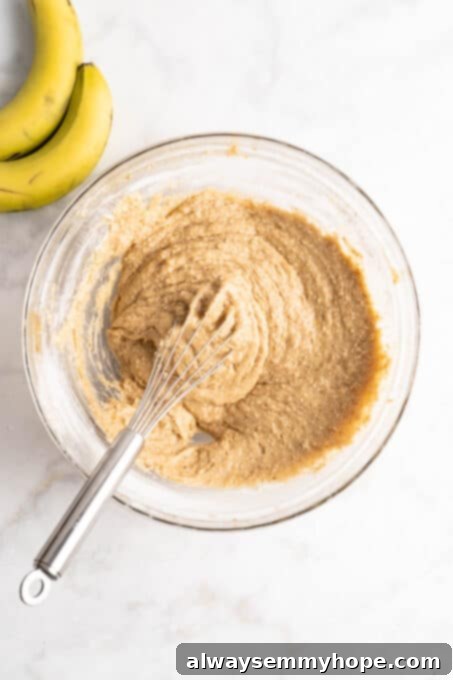 Overhead view of banana bread batter in glass bowl with whisk