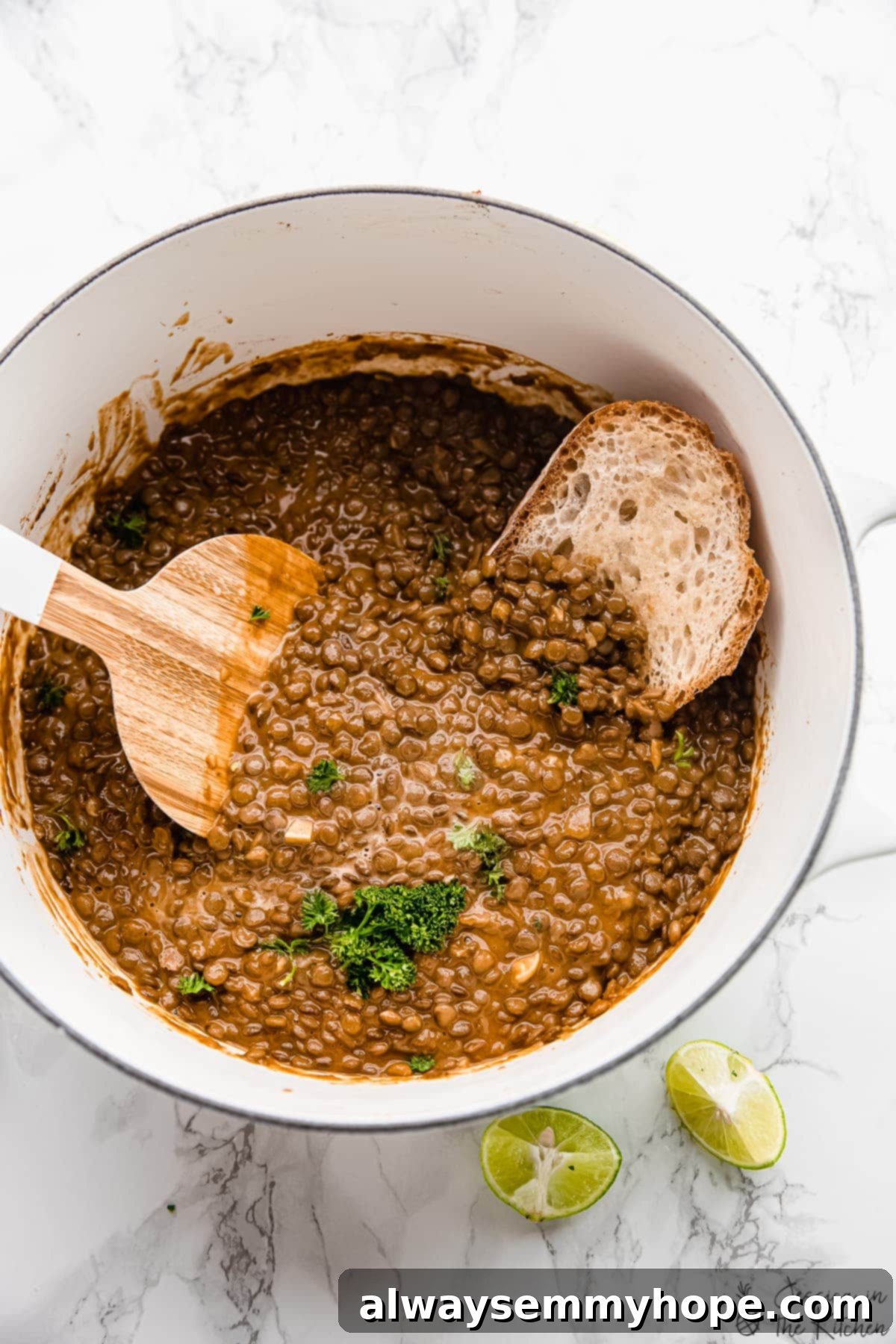 A pot of warm vegan lentil stew with a piece of crusty bread dipped into it, ready to eat.