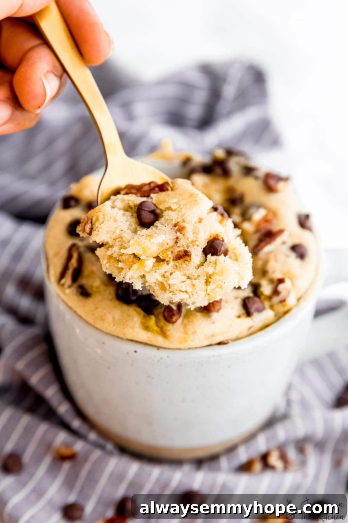 A golden spoon holds a scoop of warm, fluffy banana bread mug cake, positioned in front of the mug where the cake was cooked, highlighting its perfect texture and readiness to eat.