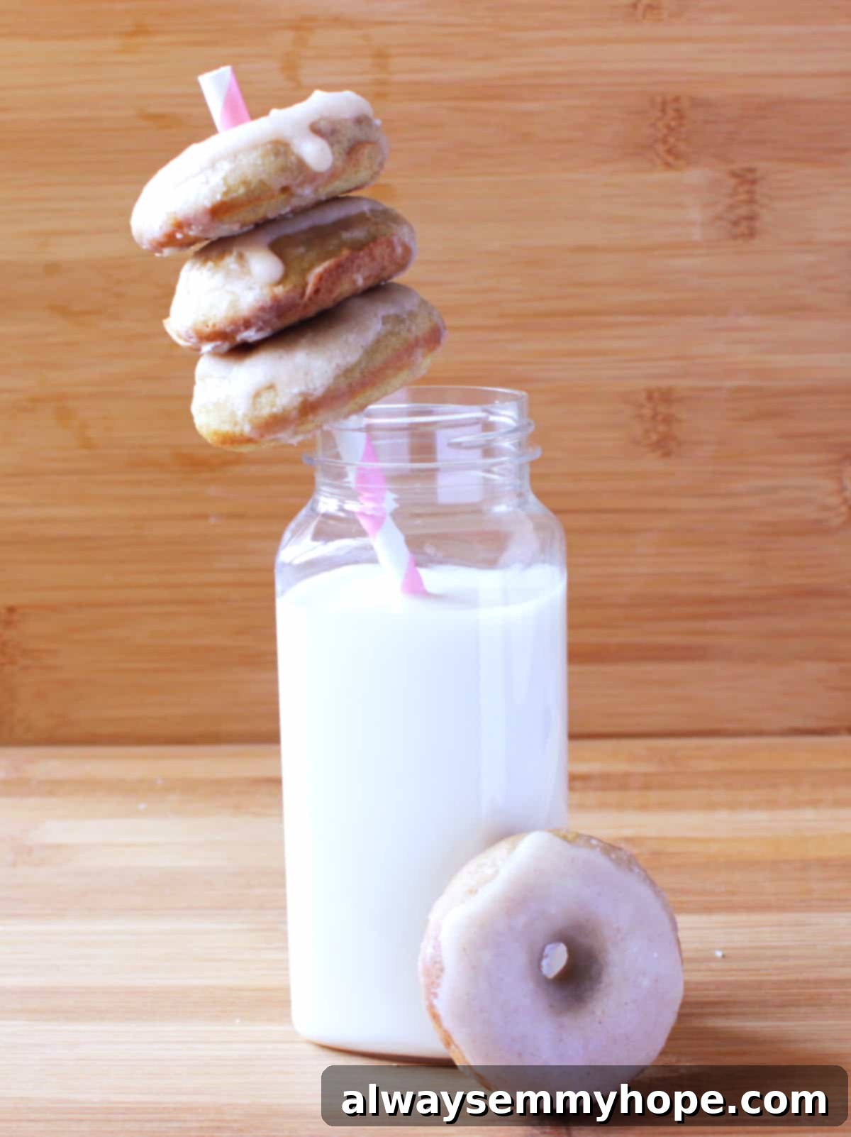 Savor the taste of homemade gingerbread doughnuts, exquisitely baked and finished with a rich cinnamon-ginger glaze, ideal for festive enjoyment! A charming close-up of gingerbread doughnuts stacked on a festive straw, accompanied by a refreshing glass of milk, evoking cozy holiday mornings.