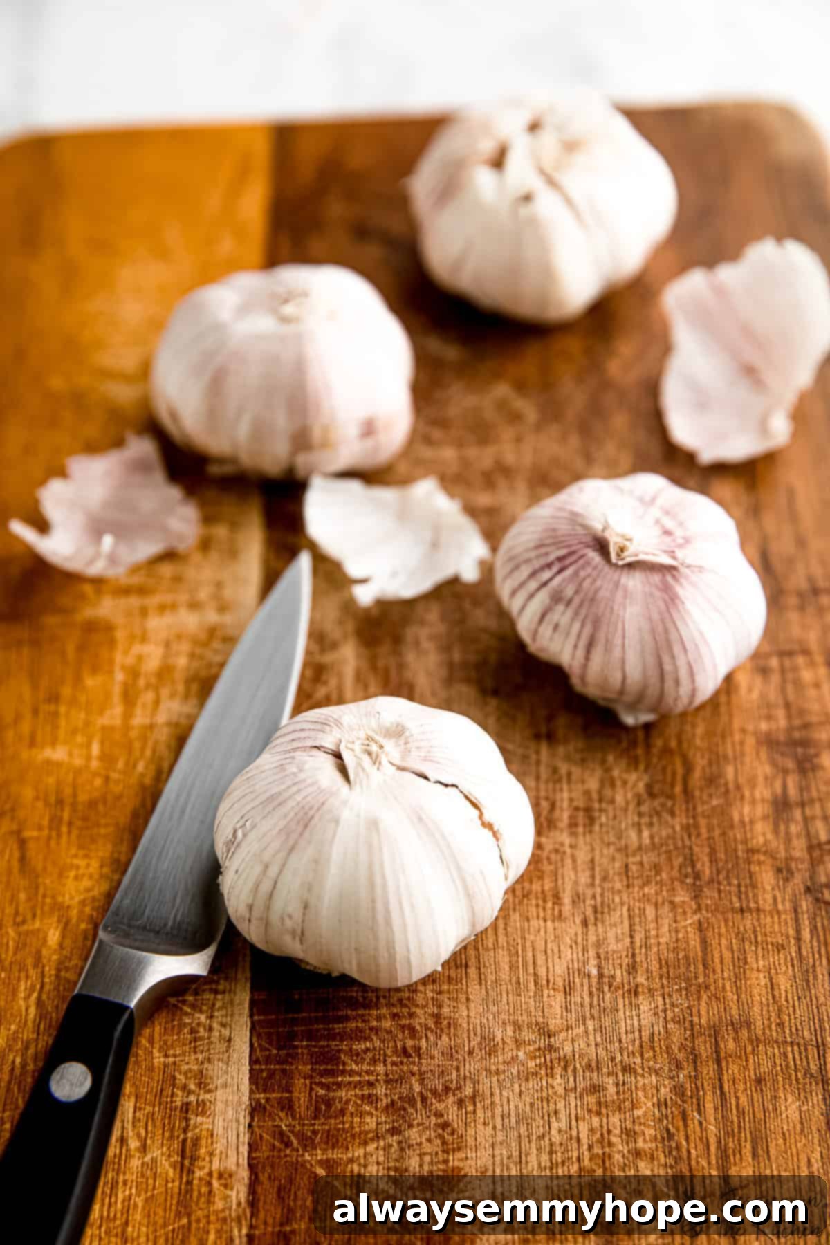 Selecting the finest garlic bulbs for roasting: a guide to fresh, plump cloves. Fresh garlic bulbs arranged on a rustic wooden board next to a chef's knife.