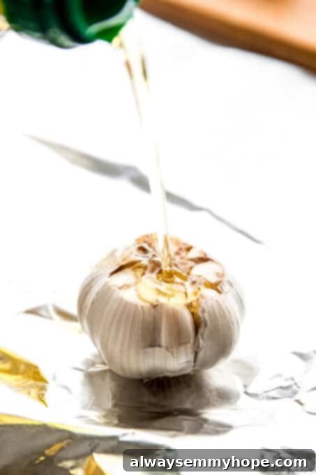 Olive oil applied to a prepared garlic bulb. A bulb of garlic, with its top cut off, being generously drizzled with olive oil before roasting.