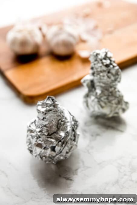 Tightly sealed garlic heads in foil, prepared for roasting. Two tightly wrapped garlic heads in aluminum foil, perfectly sealed and ready for the oven.