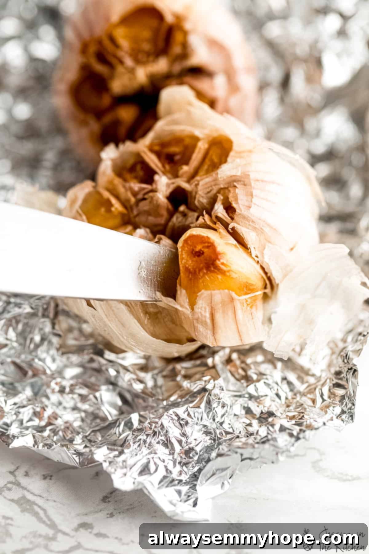 Slicing into a perfectly roasted garlic bulb to reveal soft cloves. A sharp knife gently squeezing a roasted garlic clove out of its skin, showcasing its soft, golden texture.