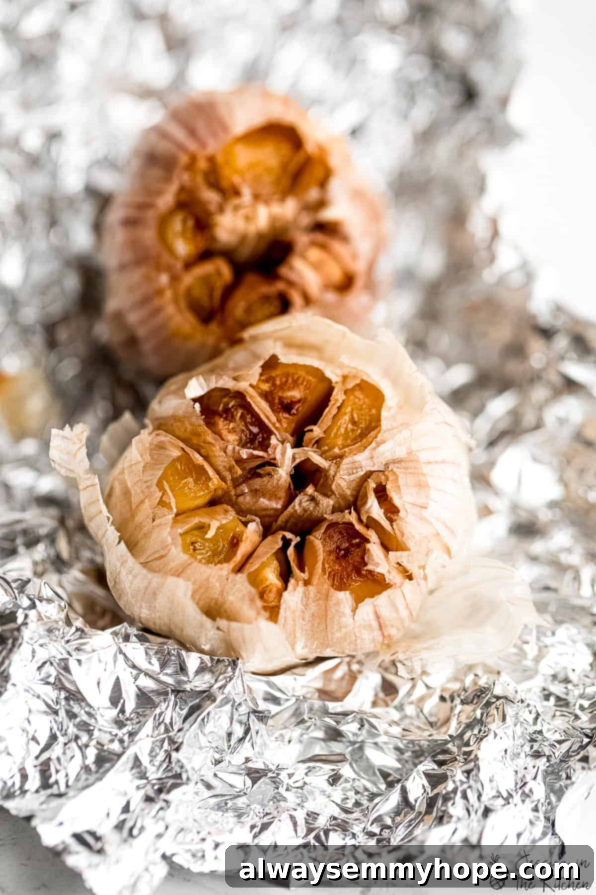 Two heads of roasted garlic on foil, perfectly caramelized. Two golden-brown heads of freshly roasted garlic resting on aluminum foil, exuding a delicious aroma.