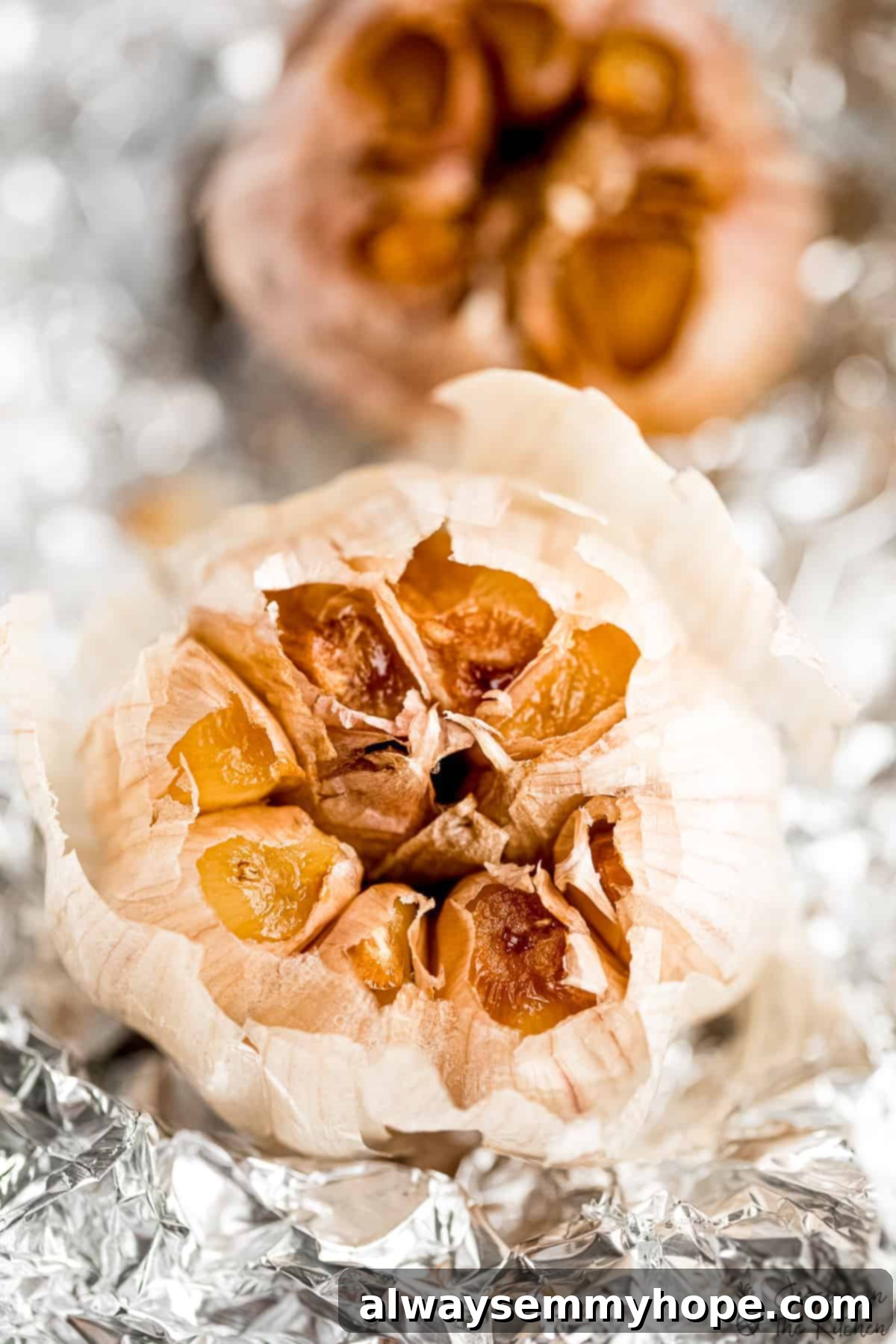 Closeup of two roasted garlic bulbs on foil, showing texture. A close-up view of two tender, golden-brown roasted garlic bulbs, still wrapped in foil and glistening with olive oil.