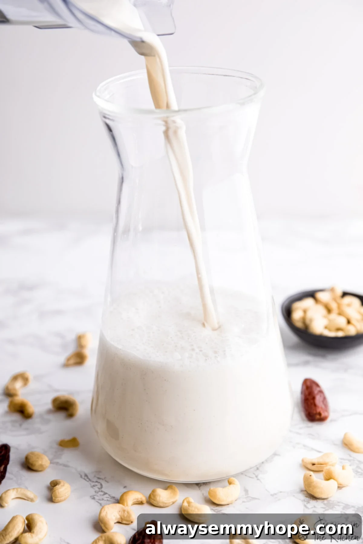 Freshly made cashew milk being poured into a clear glass jug, showcasing its smooth, white consistency.