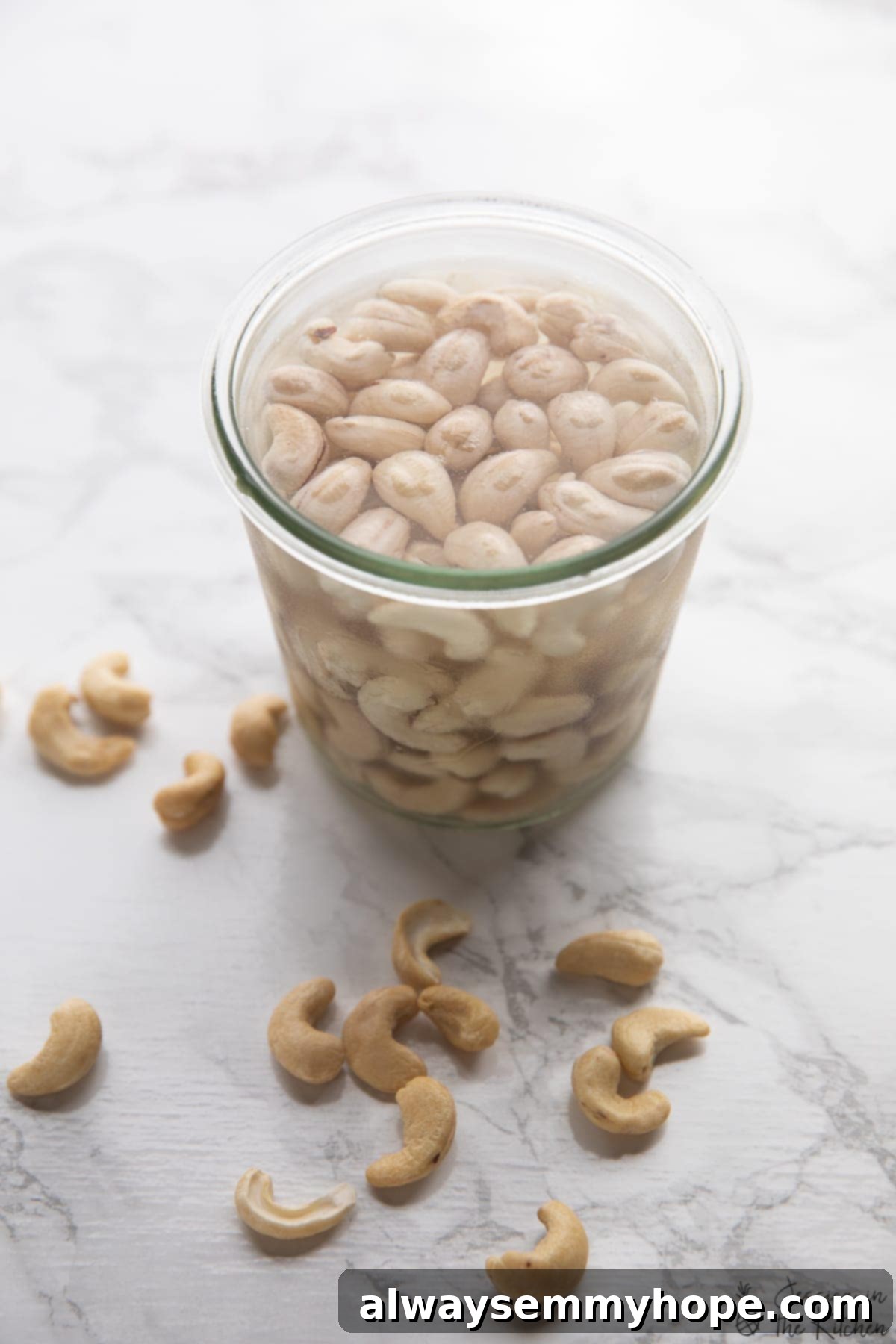Raw cashews soaking in a clear glass jar filled with water, preparing them for blending.