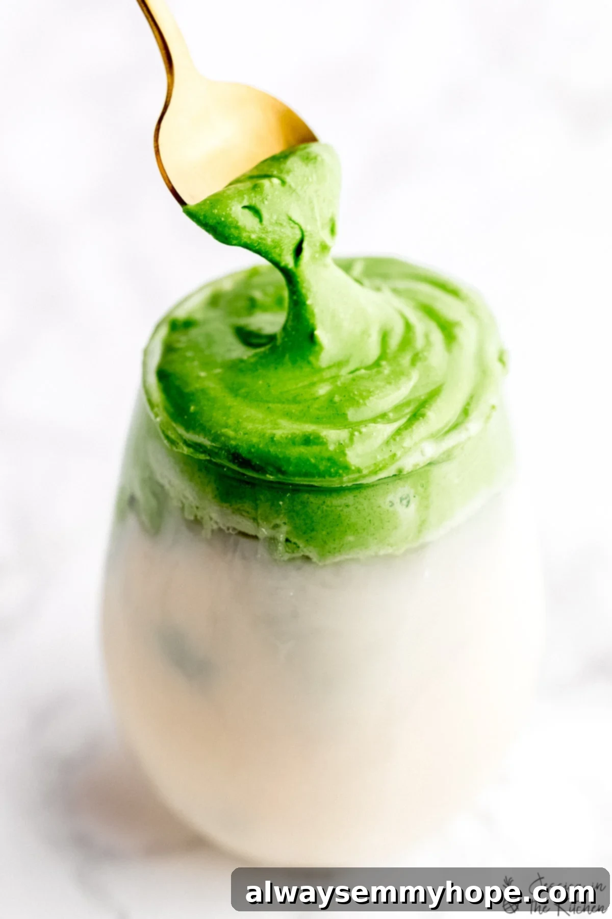 A beautifully prepared glass of whipped matcha with milk, featuring a gold spoon gently pulling through the fluffy green froth, showcasing its rich texture.