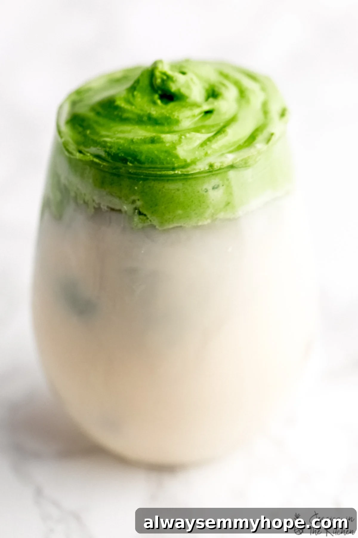 A glass filled with milk and a generous layer of vibrant whipped matcha on top, showcasing the beautiful contrast and texture.