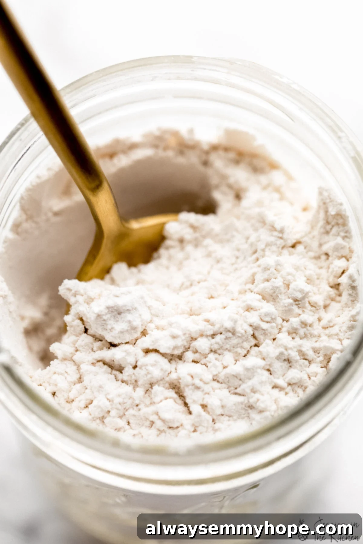 Homemade powdered sugar in a glass Weck jar, with a gold spoon embedded in the fine white powder, ready for baking or drinks.