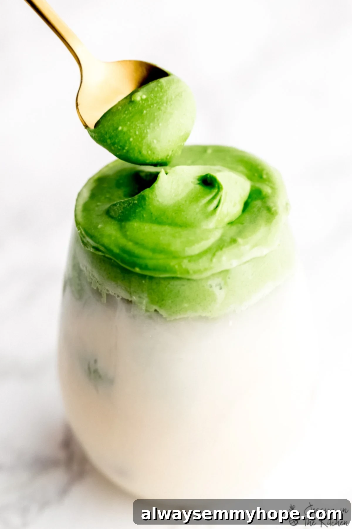 A vibrant glass of whipped matcha with milk, showing the fluffy green layer being stirred by a gold spoon, capturing the delicious fusion of flavors and textures.