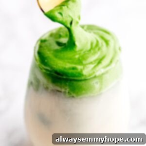 A beautifully prepared glass of whipped matcha with milk, featuring a gold spoon gently pulling through the fluffy green froth, showcasing its rich texture.