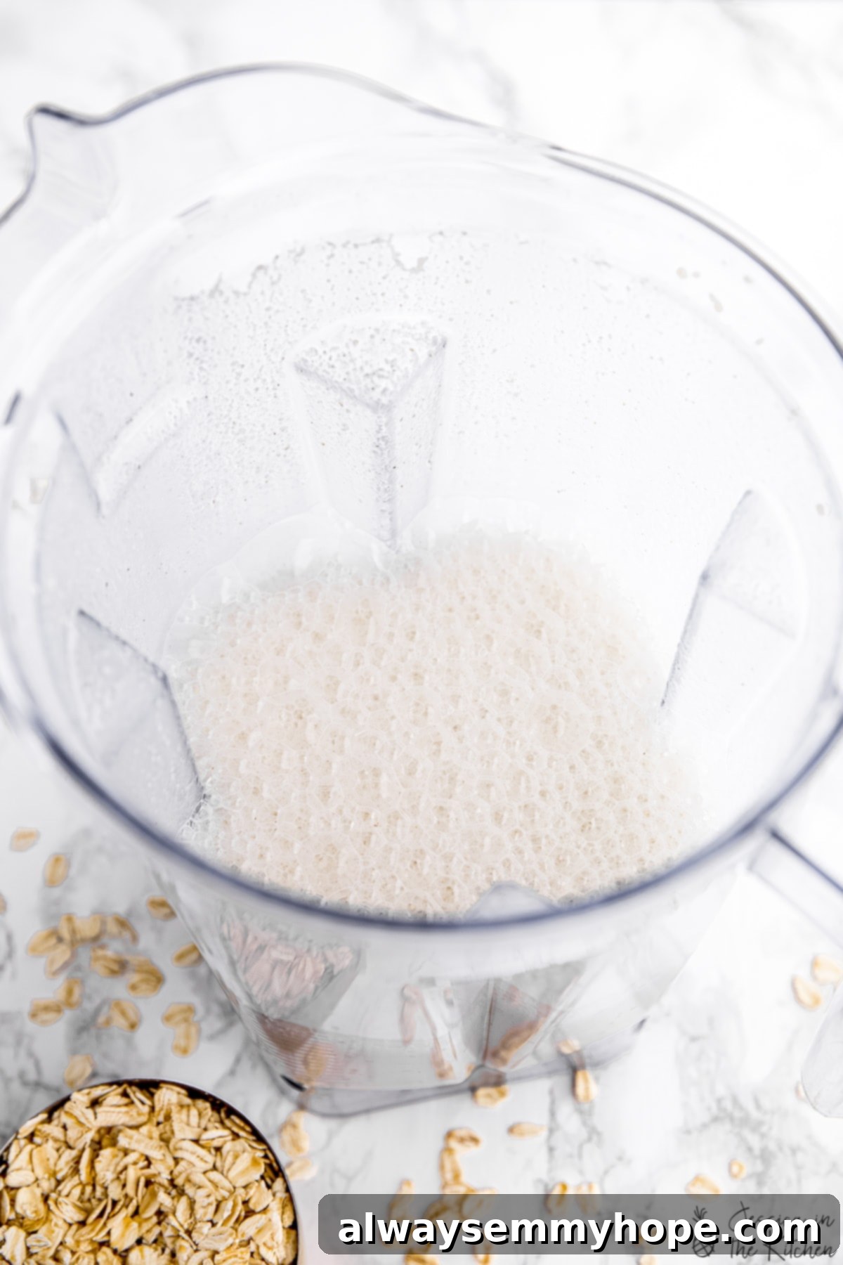 Watch your ingredients transform into rich, creamy, and delicious homemade oat milk in the blender with this easy recipe. Freshly blended homemade oat milk churning in a high-speed blender, illustrating the simplicity of the preparation process.