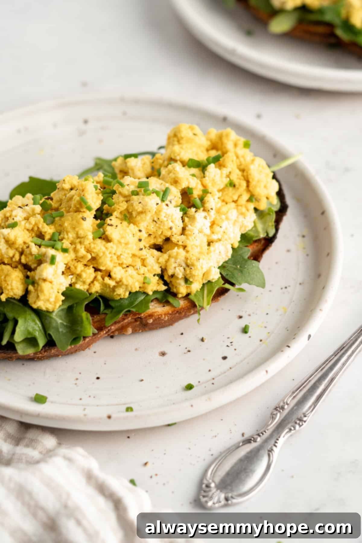 A plate of perfectly cooked, crumbled vegan tofu scramble on a slice of golden-brown toast, garnished with fresh herbs.
