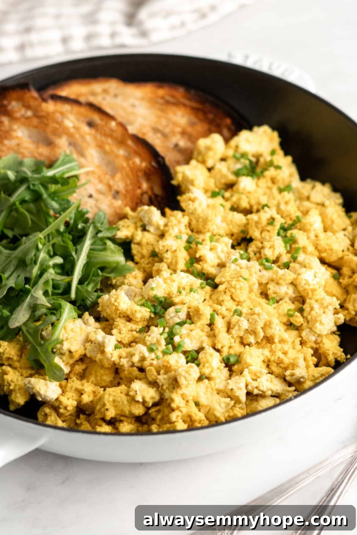 A pan featuring a generous portion of cooked vegan tofu scramble alongside perfectly browned toast, ready for serving.