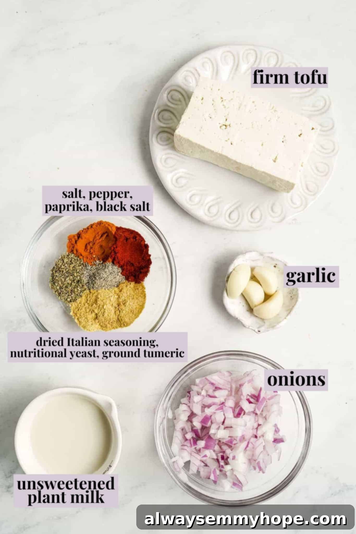 A vibrant selection of fresh ingredients including pressed tofu, red onion, garlic, and various spices laid out for making vegan tofu scramble.