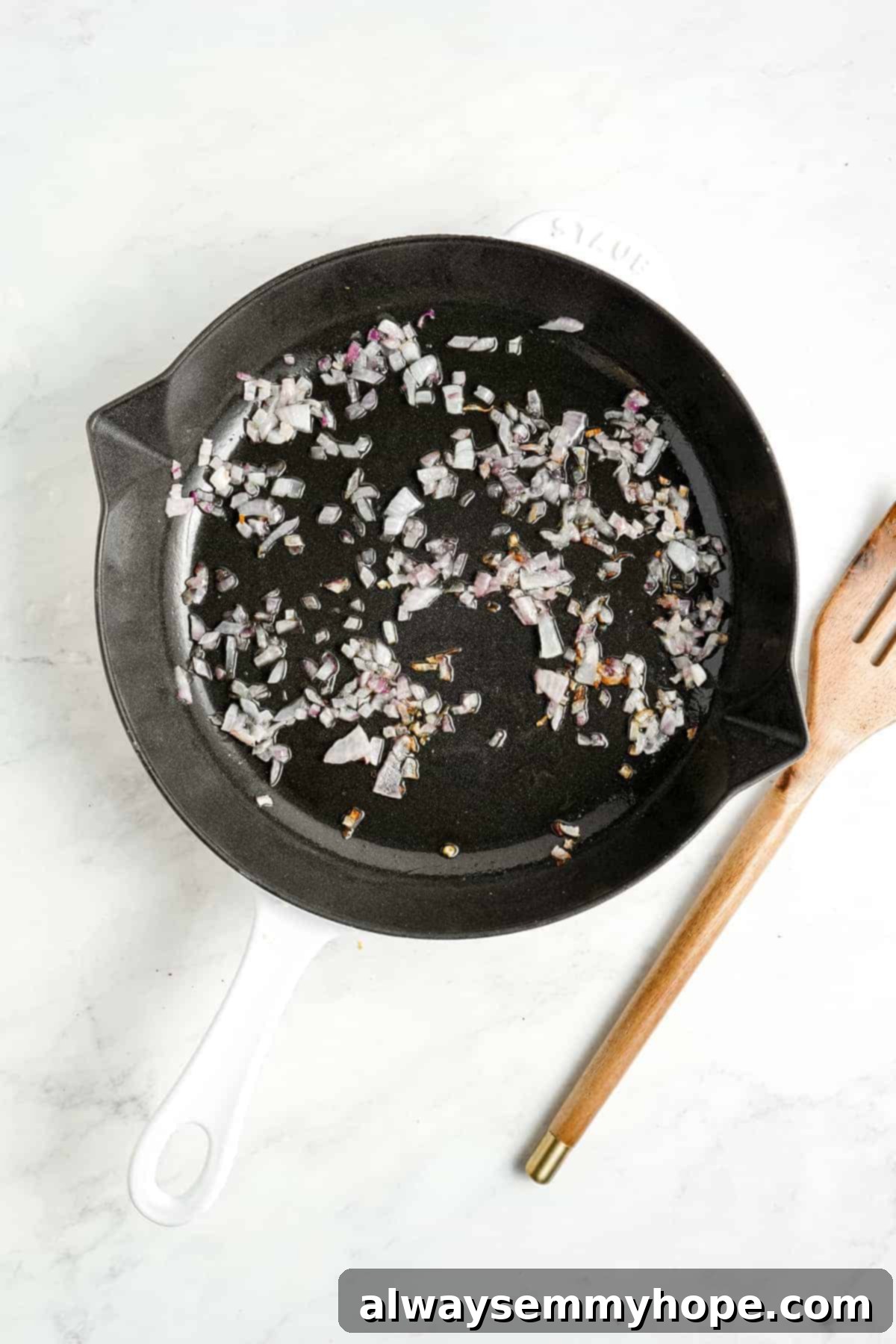 Finely chopped red onion and minced garlic gently sautéing in a pan with hot coconut oil, releasing their aromatic flavors.