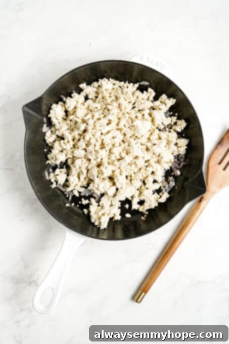 Crumbled pressed tofu mixed with sautéed onion and garlic in a pan, before seasoning.