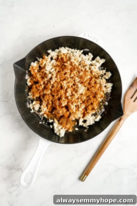 Crumbled tofu in a pan, generously coated with a vibrant blend of dry spices and seasonings.