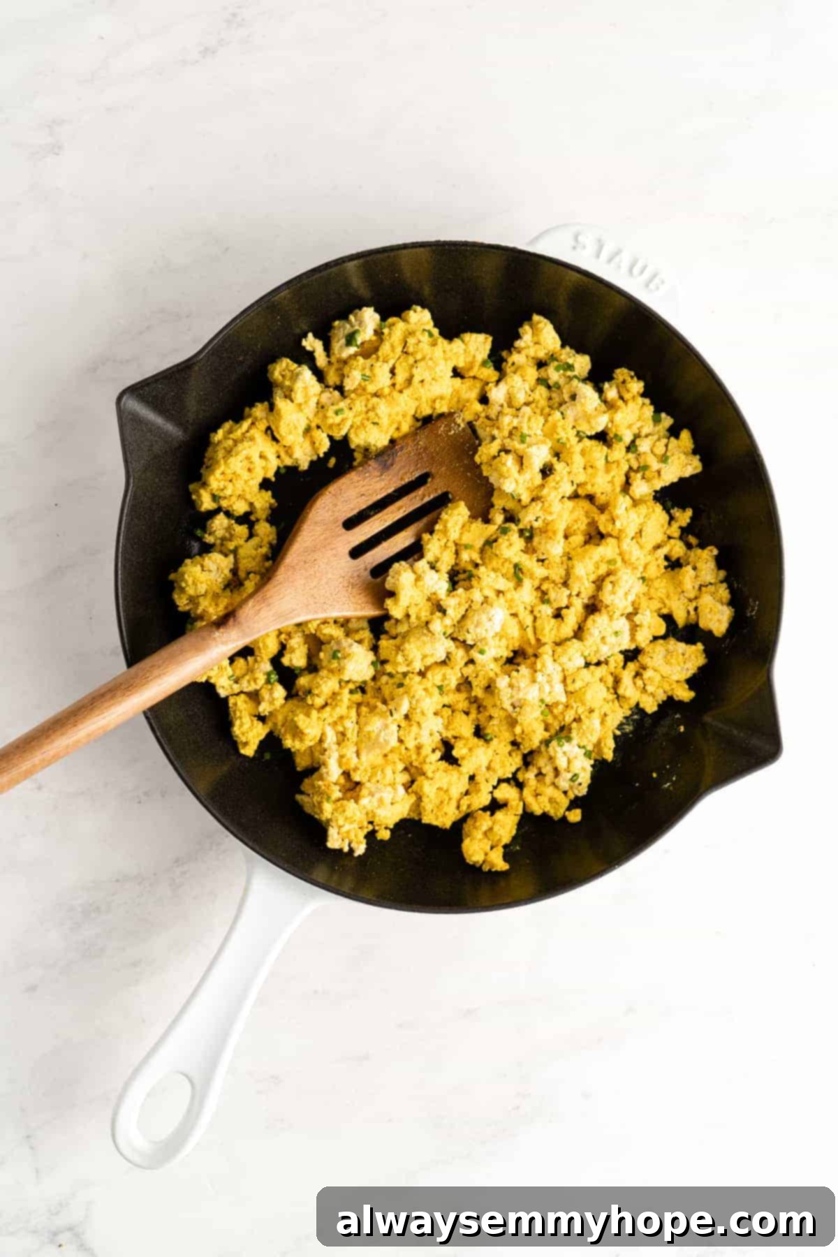 Fluffy, seasoned crumbled tofu cooking in a pan with milk, achieving a saucy texture.