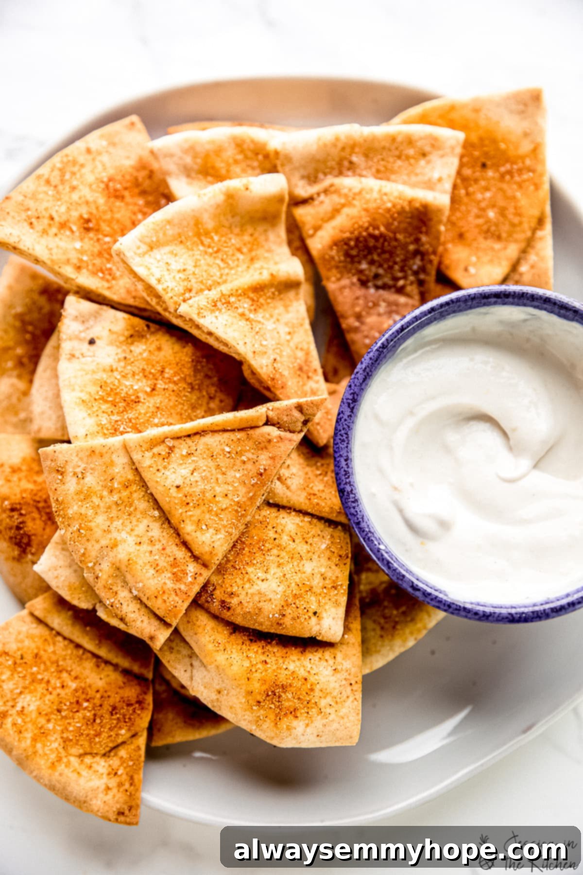 A plate stacked high with golden homemade pita chips, perfectly crispy, with a bowl of creamy dip beside it.