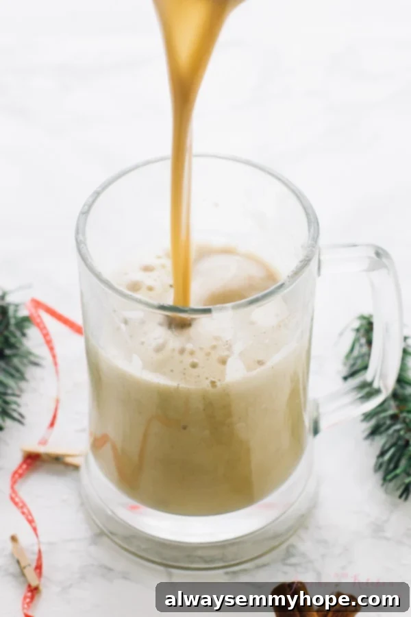 This Boozy Christmas Spiced Eggnog will become your new favourite eggnog! It's warm, frothy, and flavored with spiced rum! A glass mug filled with frothy Boozy Christmas Spiced Eggnog, garnished with a sprinkle of nutmeg, being poured.